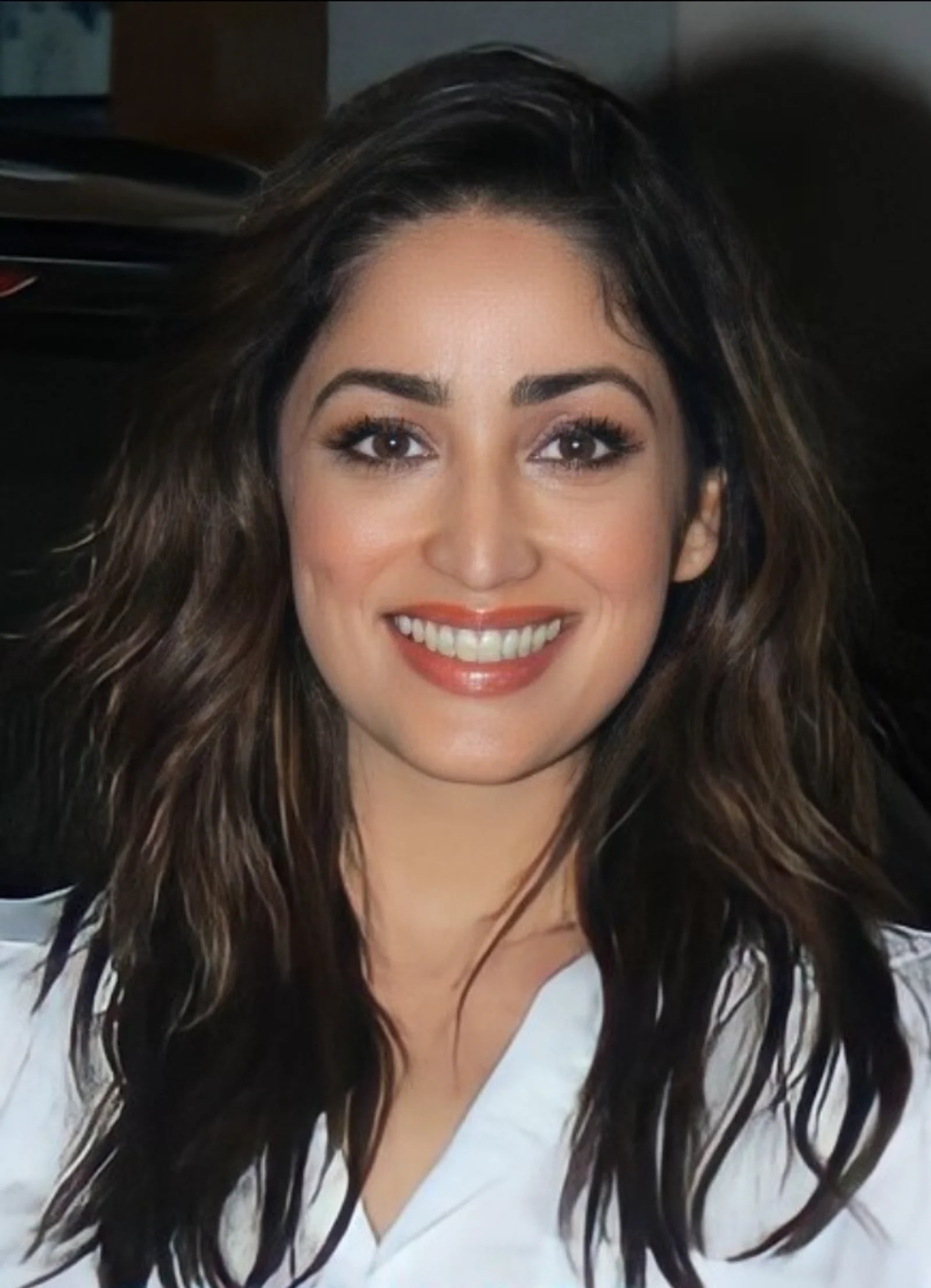 Close-up portrait of Yami Gautam smiling radiantly, showing her dimples and long wavy dark hair, wearing a light top.