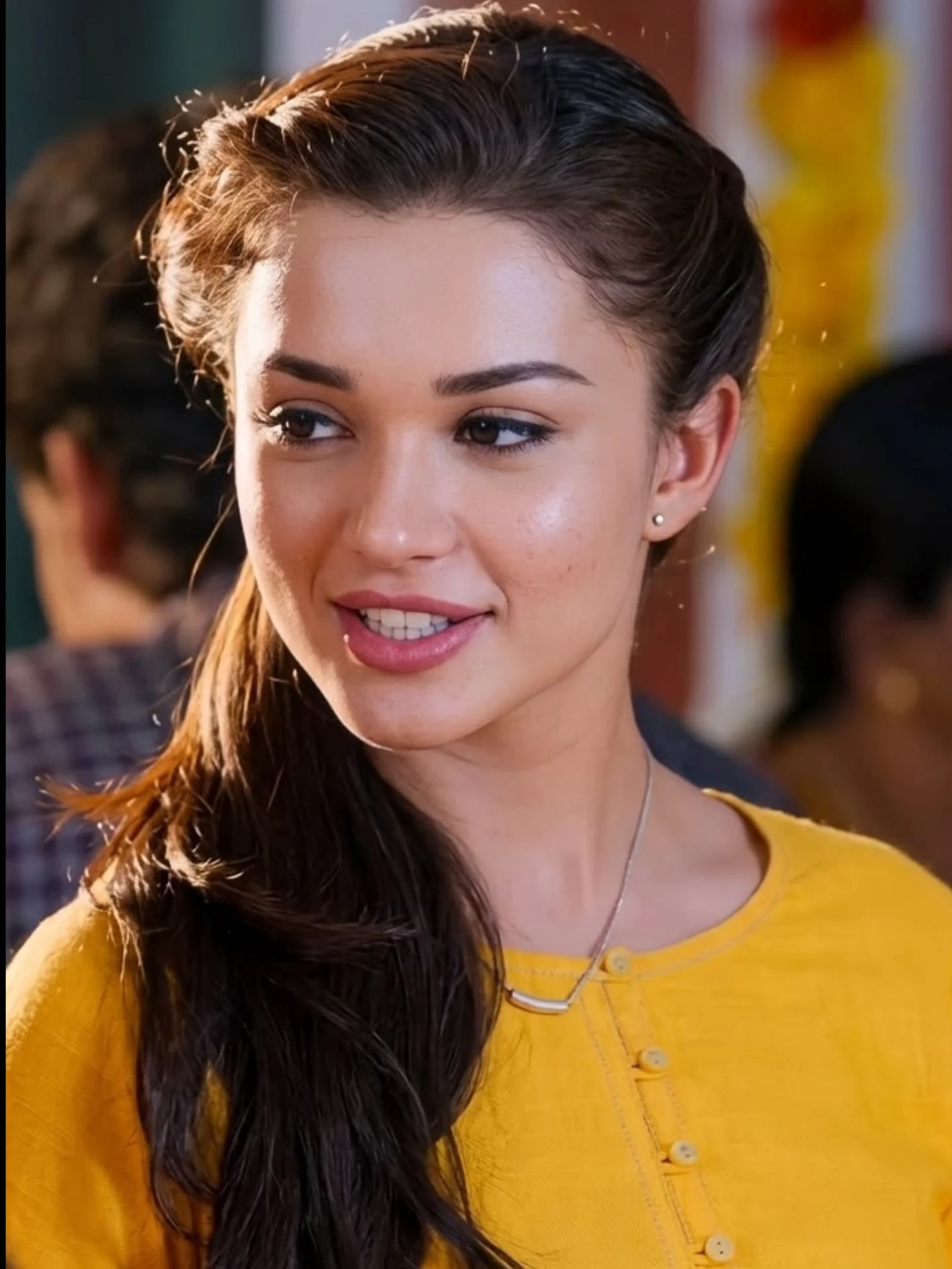 Amy Jackson smiling, wearing a yellow top and silver necklace, with her hair pulled back.