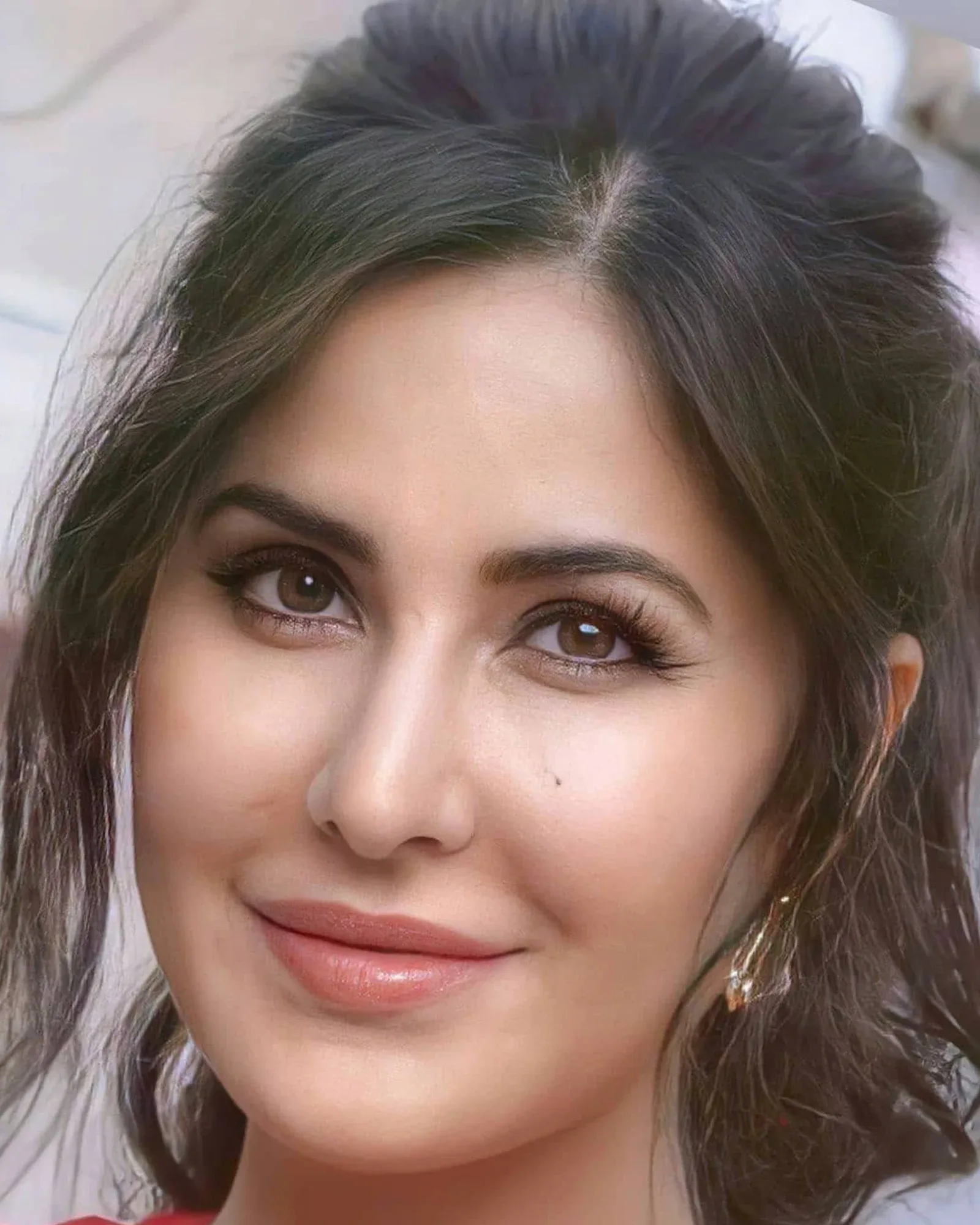 Close-up portrait of Katrina Kaif smiling softly, with dark brown hair, expressive brown eyes, glossy nude-pink lips, and a small beauty mark below her right eye.