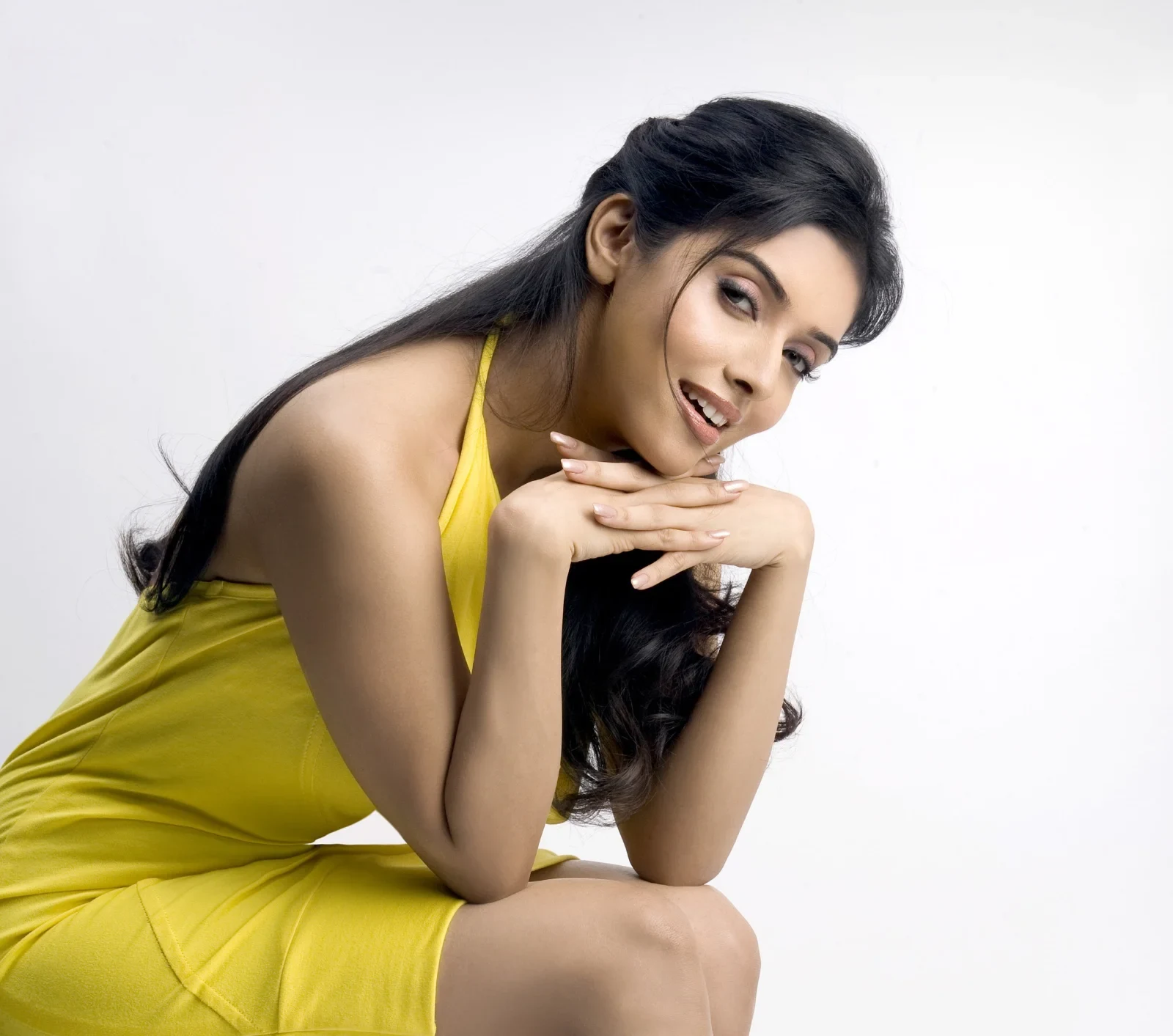Asin, an Indian actress, smiling brightly while posing in a yellow halter-neck dress against a white background.