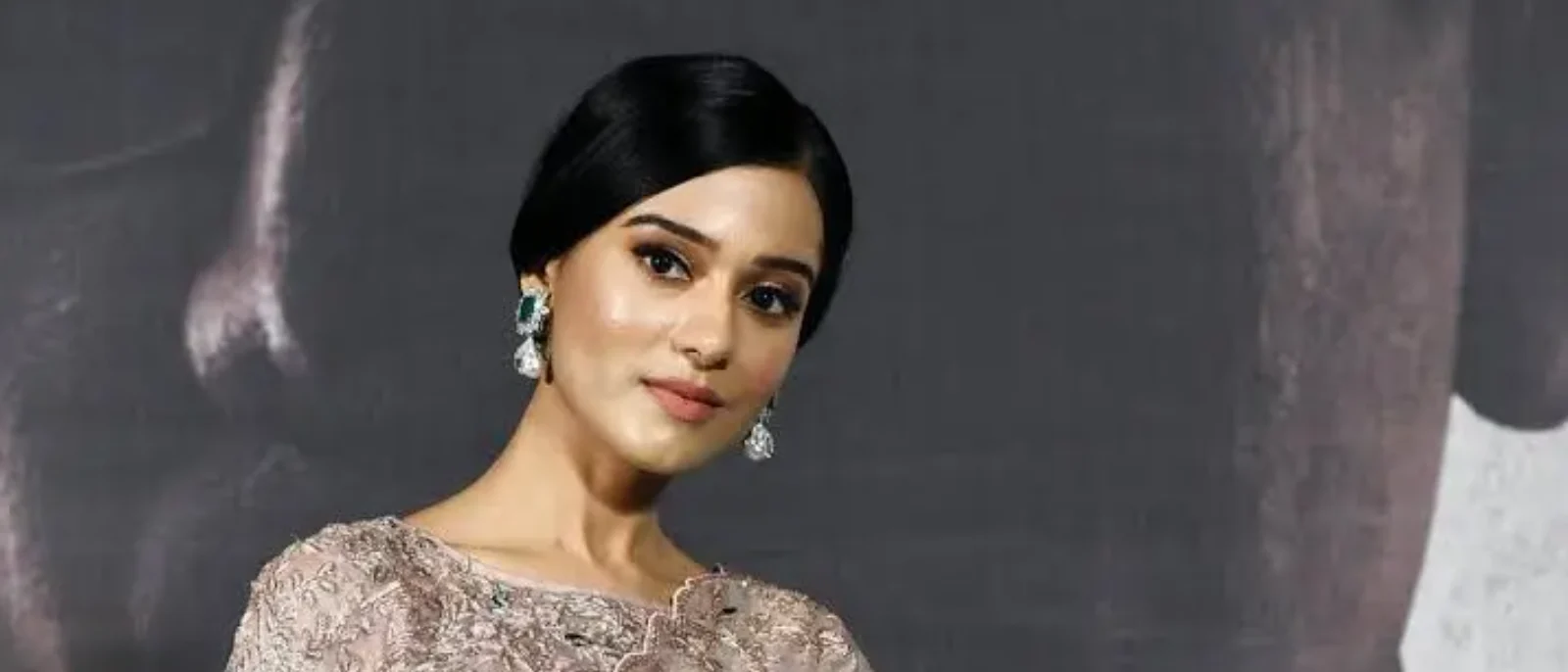 Amrita Rao, an Indian actress, posing elegantly in a blush pink embroidered outfit with emerald and diamond drop earrings, her dark hair neatly styled.
