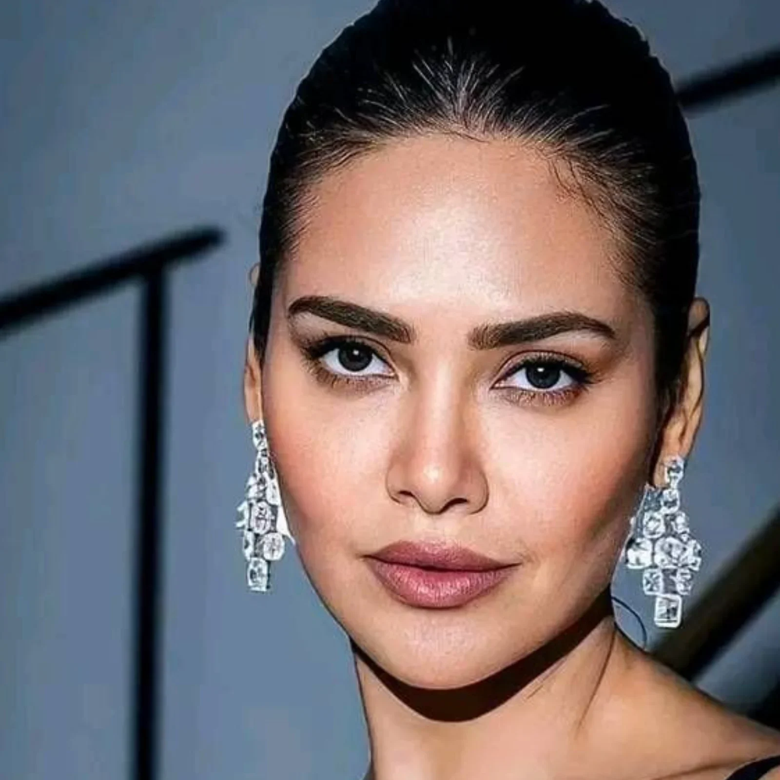 Close-up portrait of Esha Gupta, an Indian actress, with dark hair pulled back, wearing large, sparkling chandelier diamond earrings, looking directly at the camera with a serene expression.