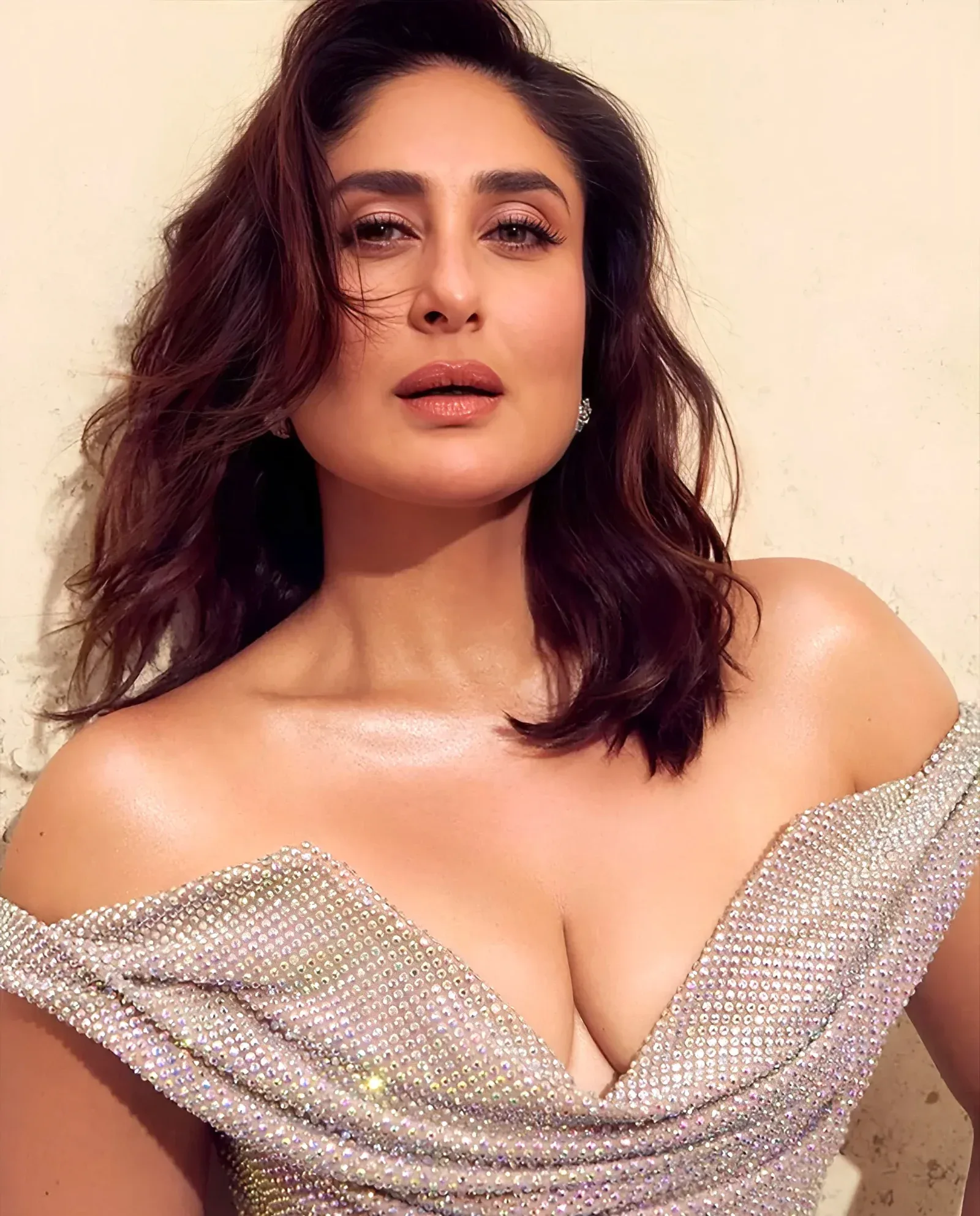 Kareena Kapoor, a Bollywood actress, posing in a sparkling silver off-shoulder gown with a deep V-neck, her dark wavy hair framing her face, and a confident expression.