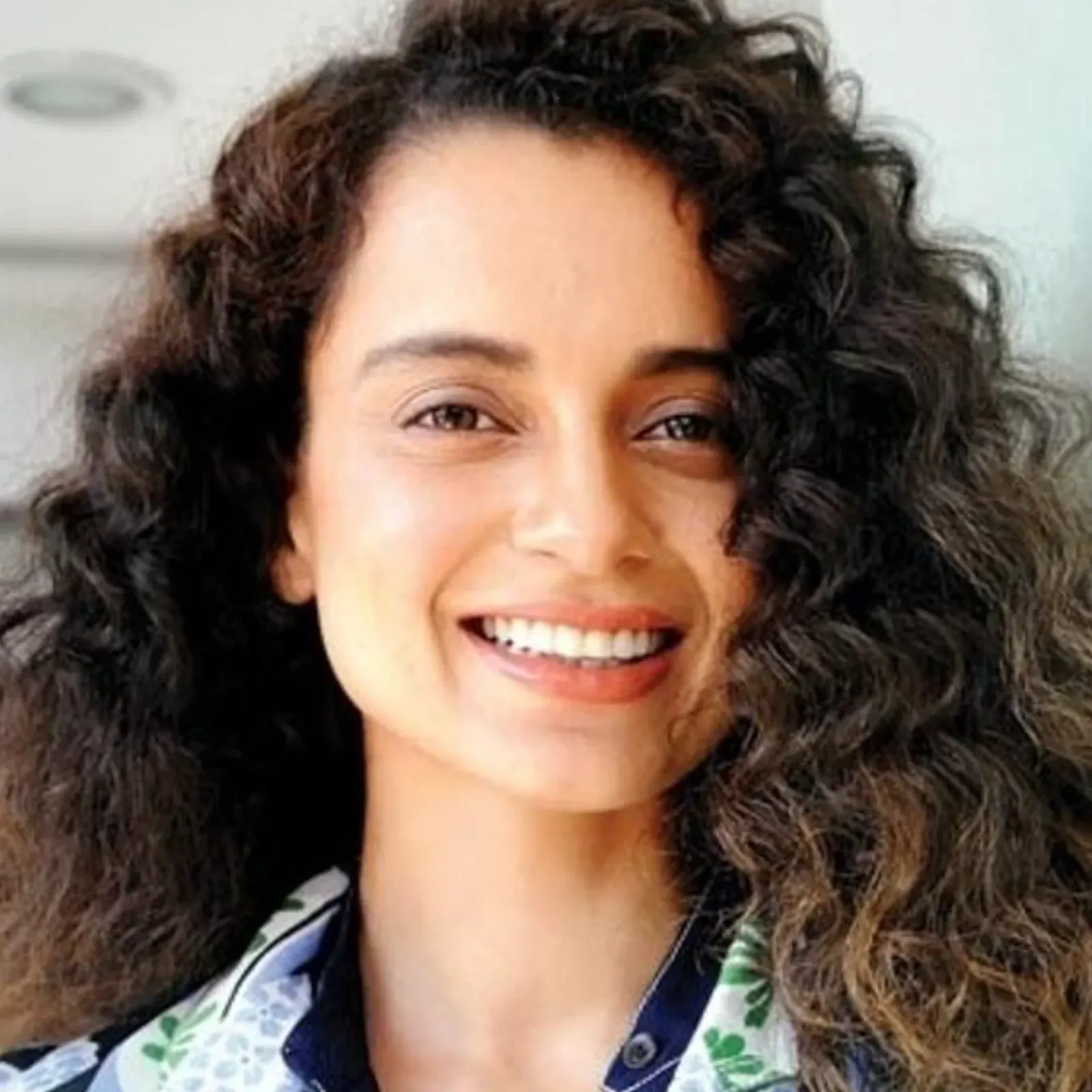 Kangana Ranaut smiling with curly hair and floral outfit.