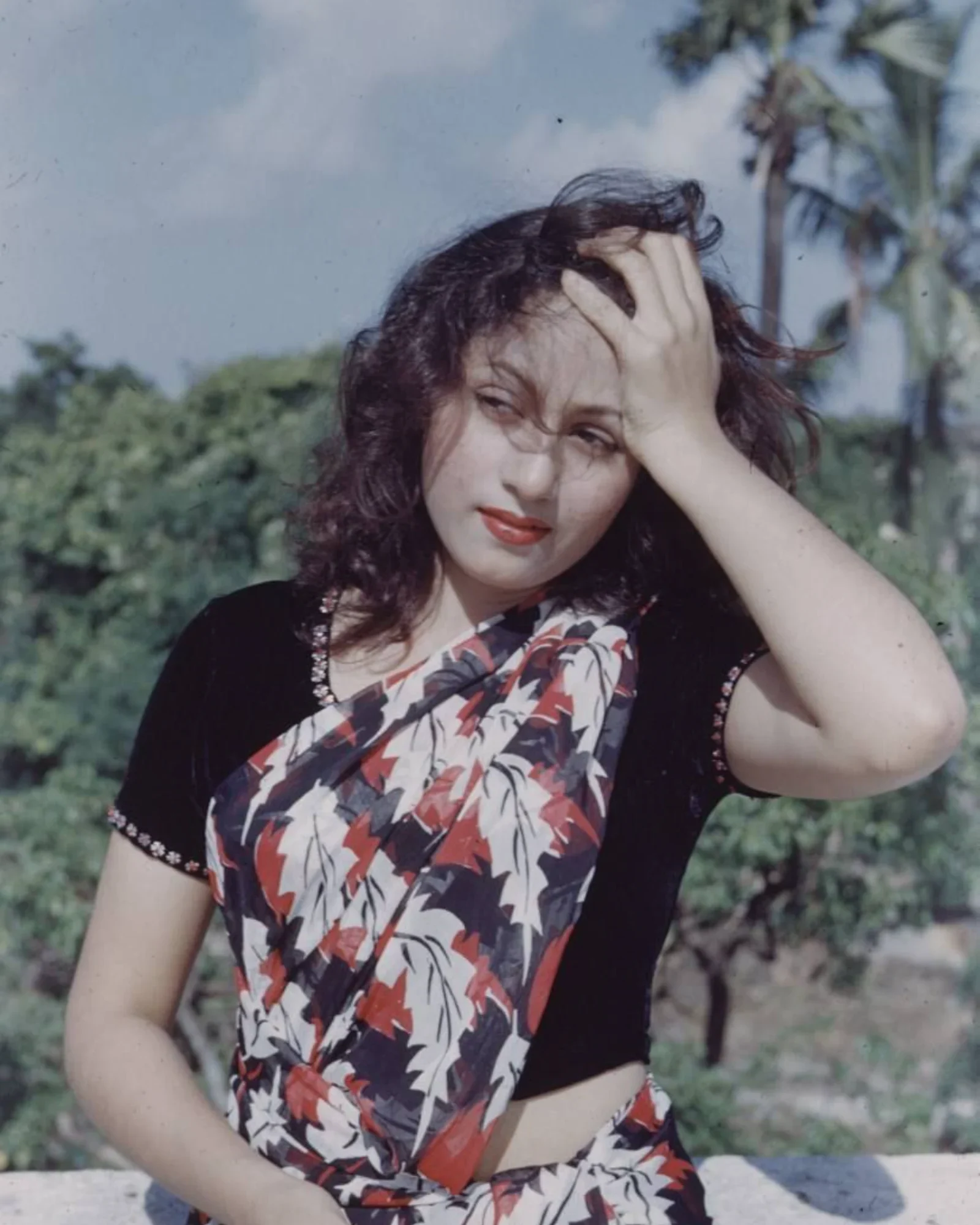 Madhubala wearing a floral saree outdoors, with a serene expression.