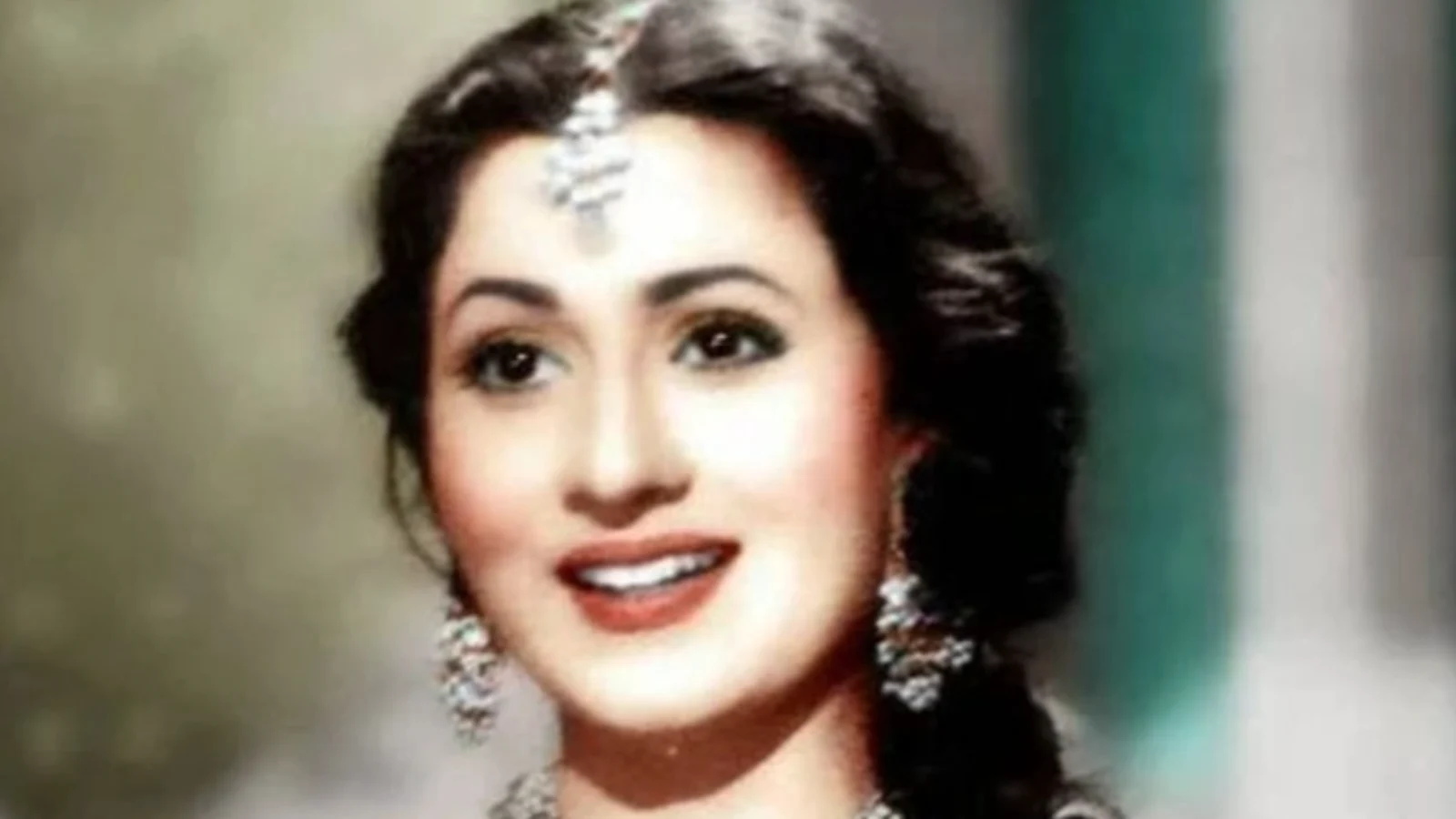 Close-up portrait of Madhubala, a classic Indian actress, smiling and wearing traditional maang tikka and elaborate dangling earrings.
