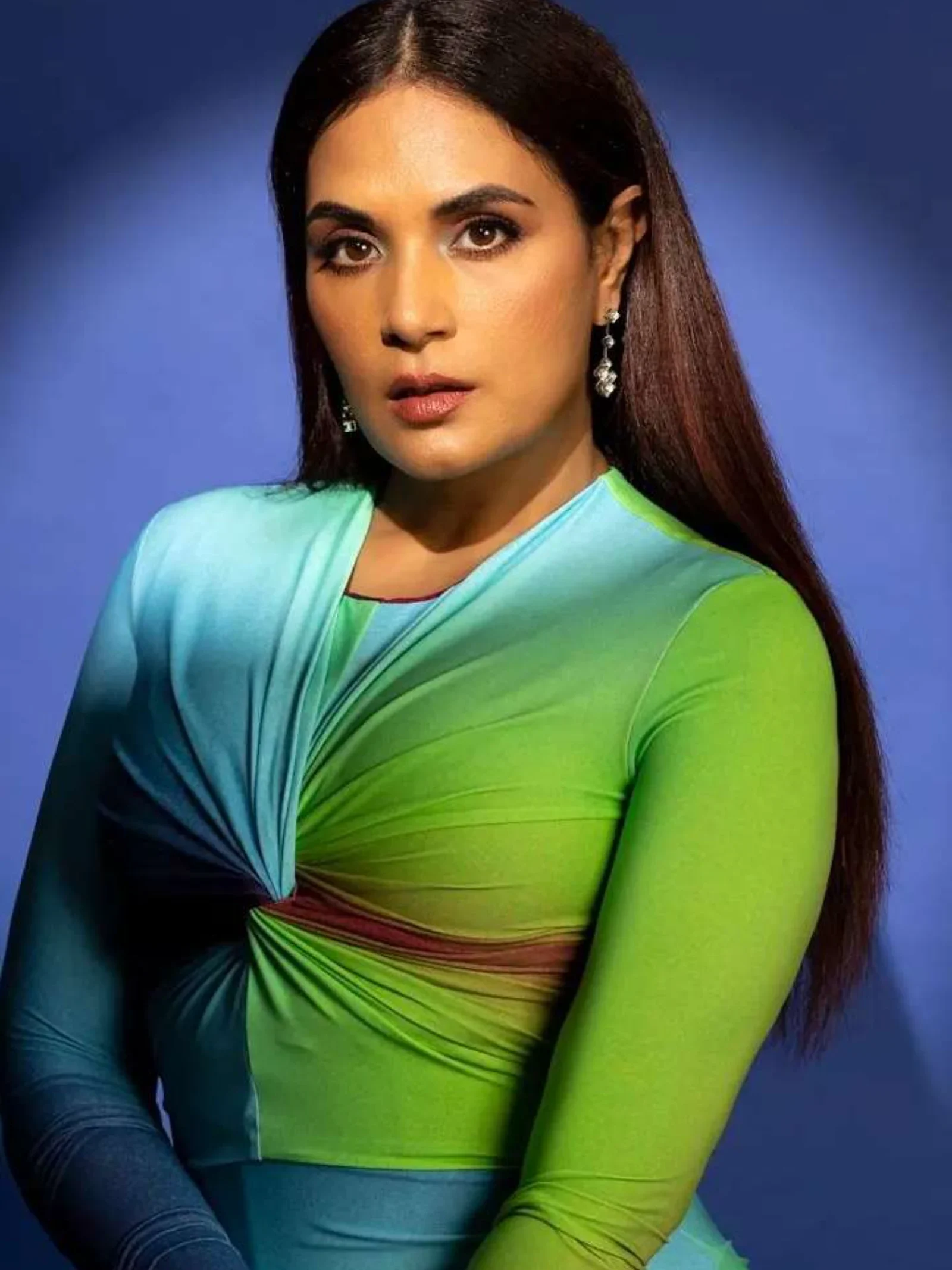 Richa Chadha posing in a vibrant green and blue gradient dress against a blue background