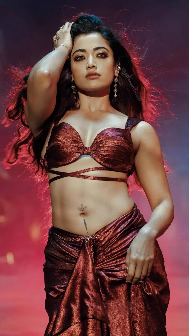 Rashmika Mandanna posing in a metallic crop top and draped skirt showing her midriff