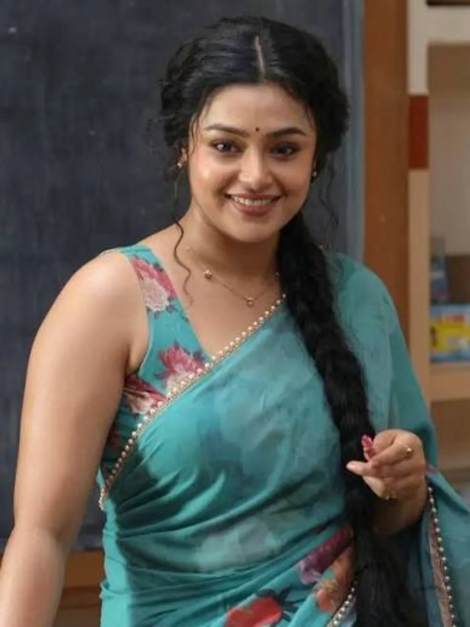 Mokksha dressed as Meenu Mam in a teal saree smiling.