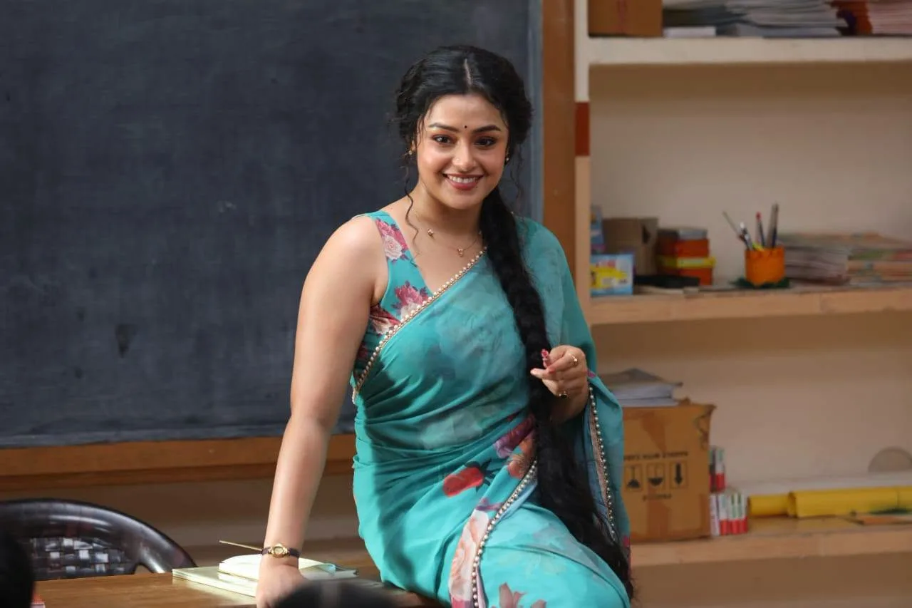 Mokksha smiling in a turquoise floral saree as Meenu Mam in a classroom