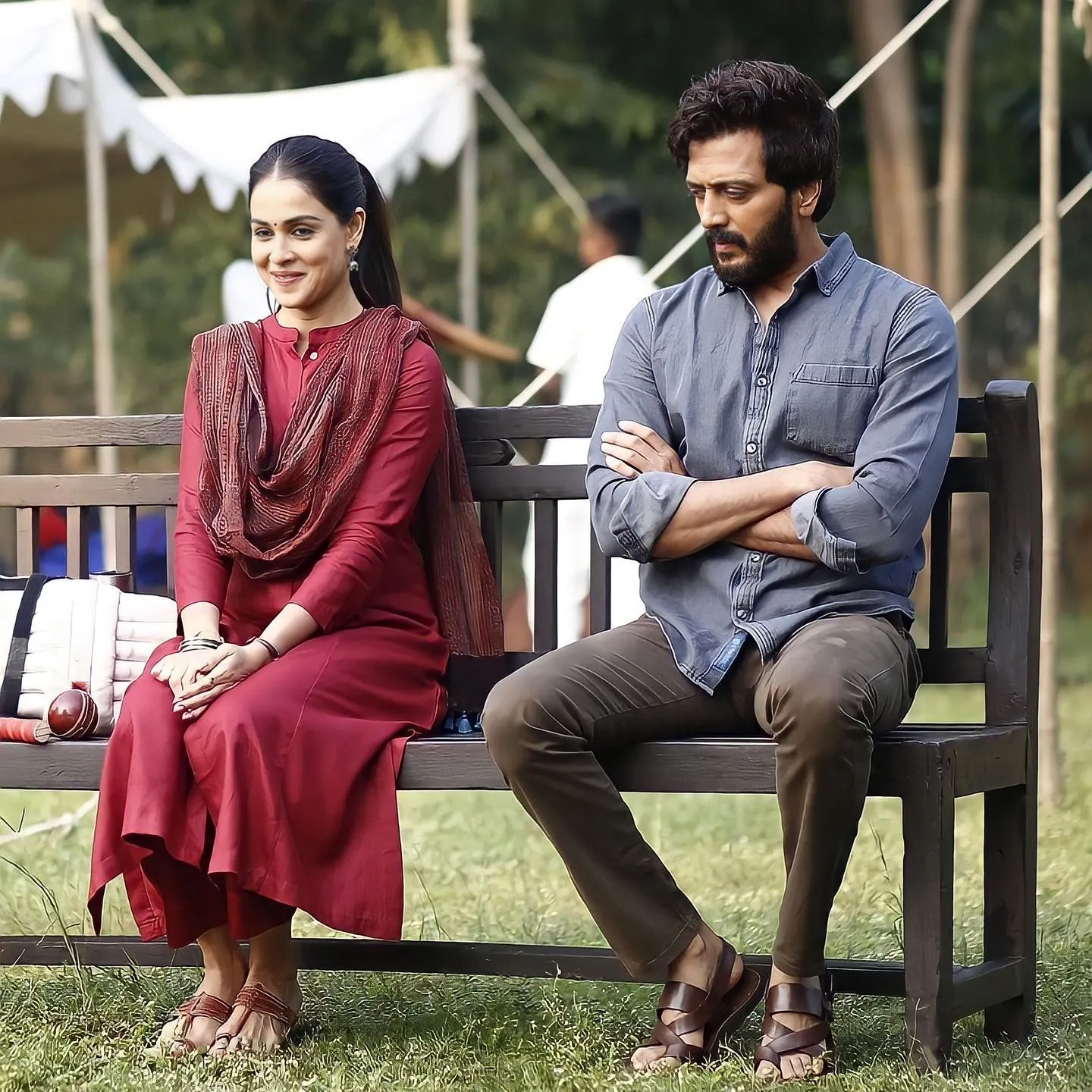 Genelia D'Souza wearing a red traditional kurta seated next to Riteish Deshmukh on a bench in a movie still from Ved.