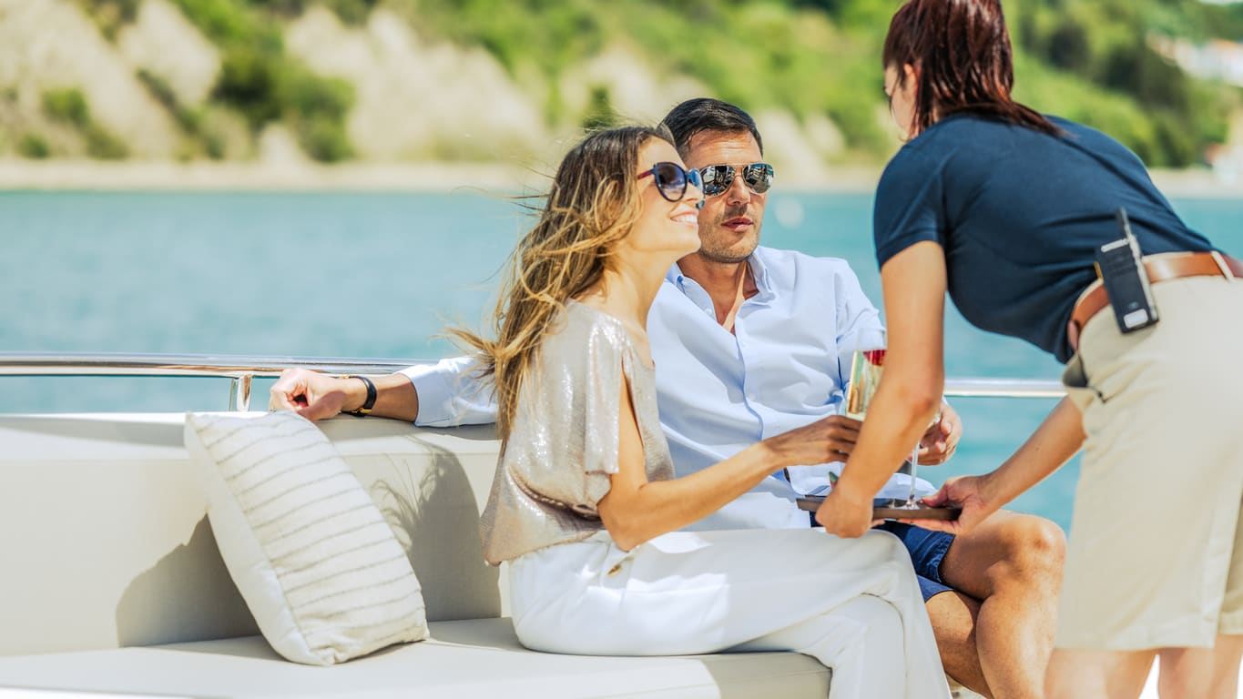 Happy smiling woman and her partner getting glass of champagne from female crew member. Luxury vacation at sea.