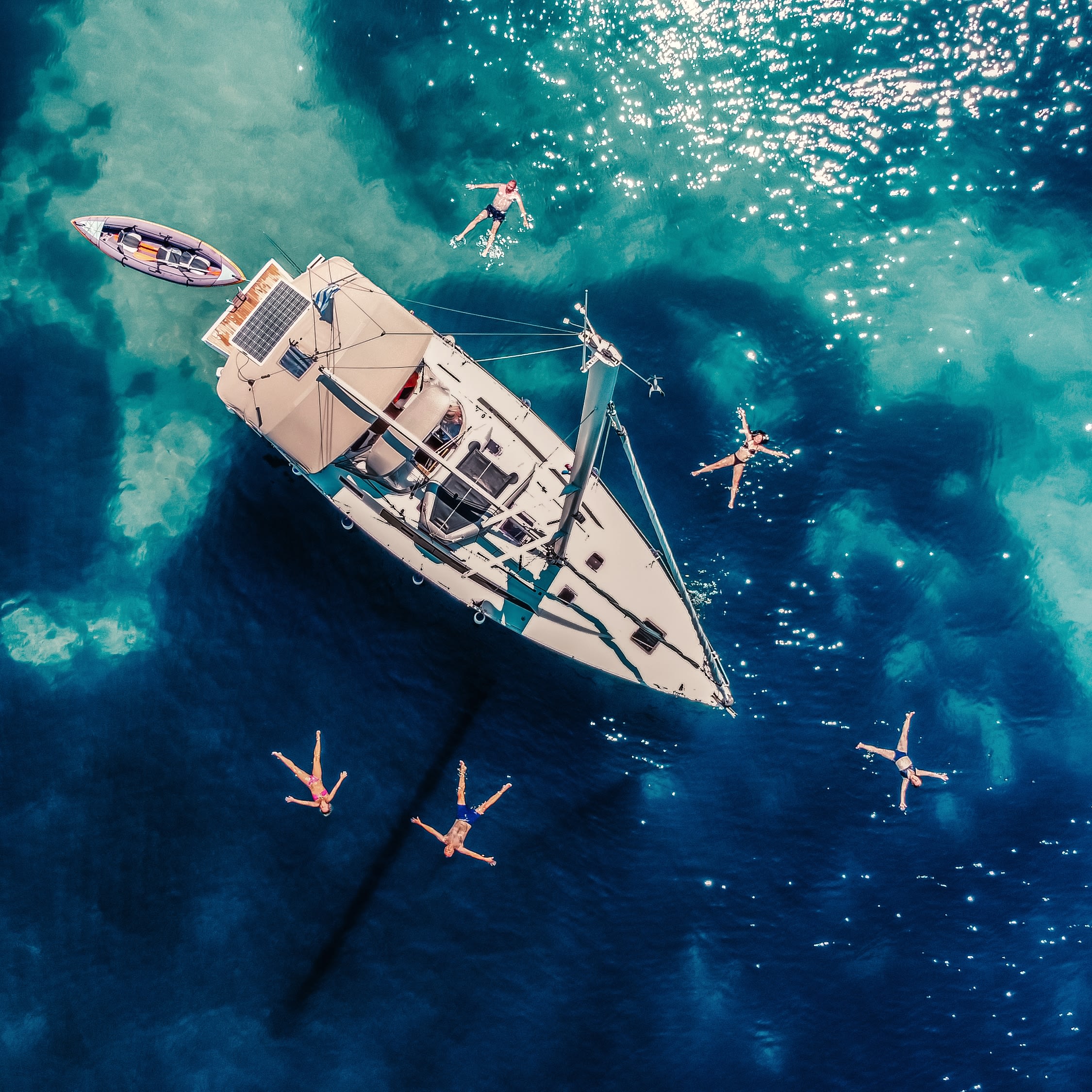 High-angle view of distant people swimming by modern sailboat on the sea