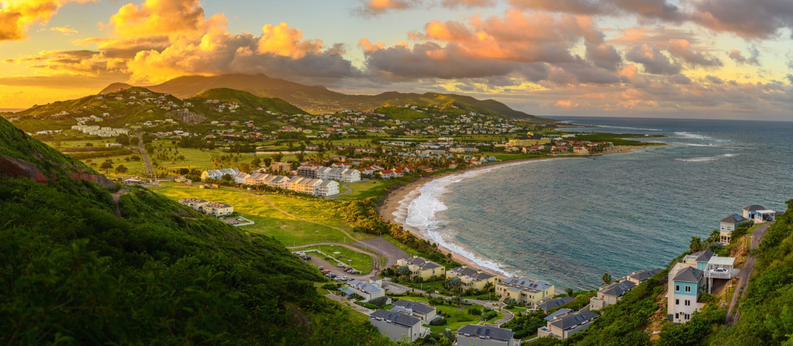 Panorama of Saint Kitts and its capital Basseterre during sunset, beautiful green mountains and a beach in paradise caribbean island with amazing green and orange colors