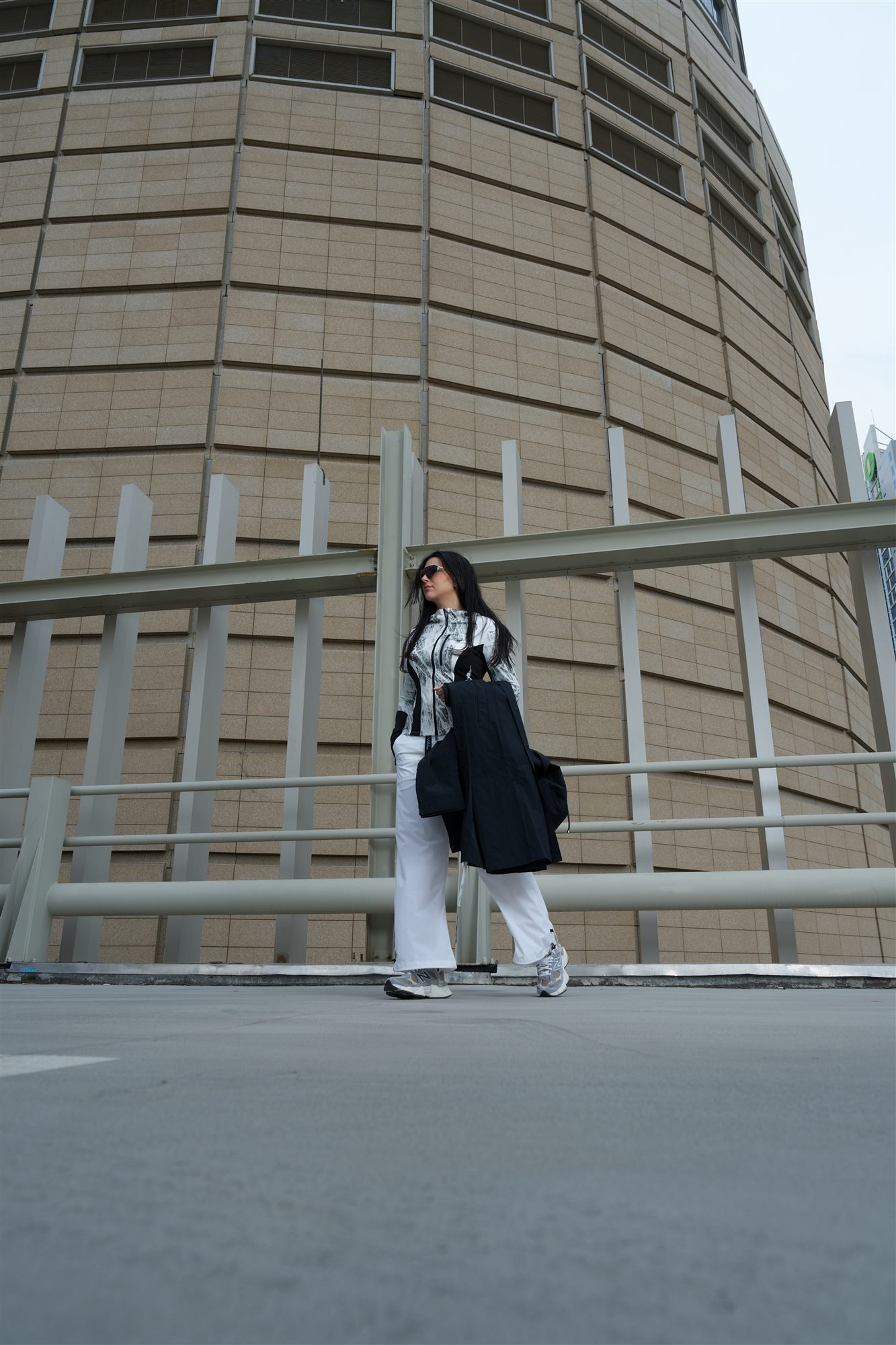 A figure in considered outerwear walking past a curved tower facade in cool GCC daylight, the place NeoSpherium was imagined from.