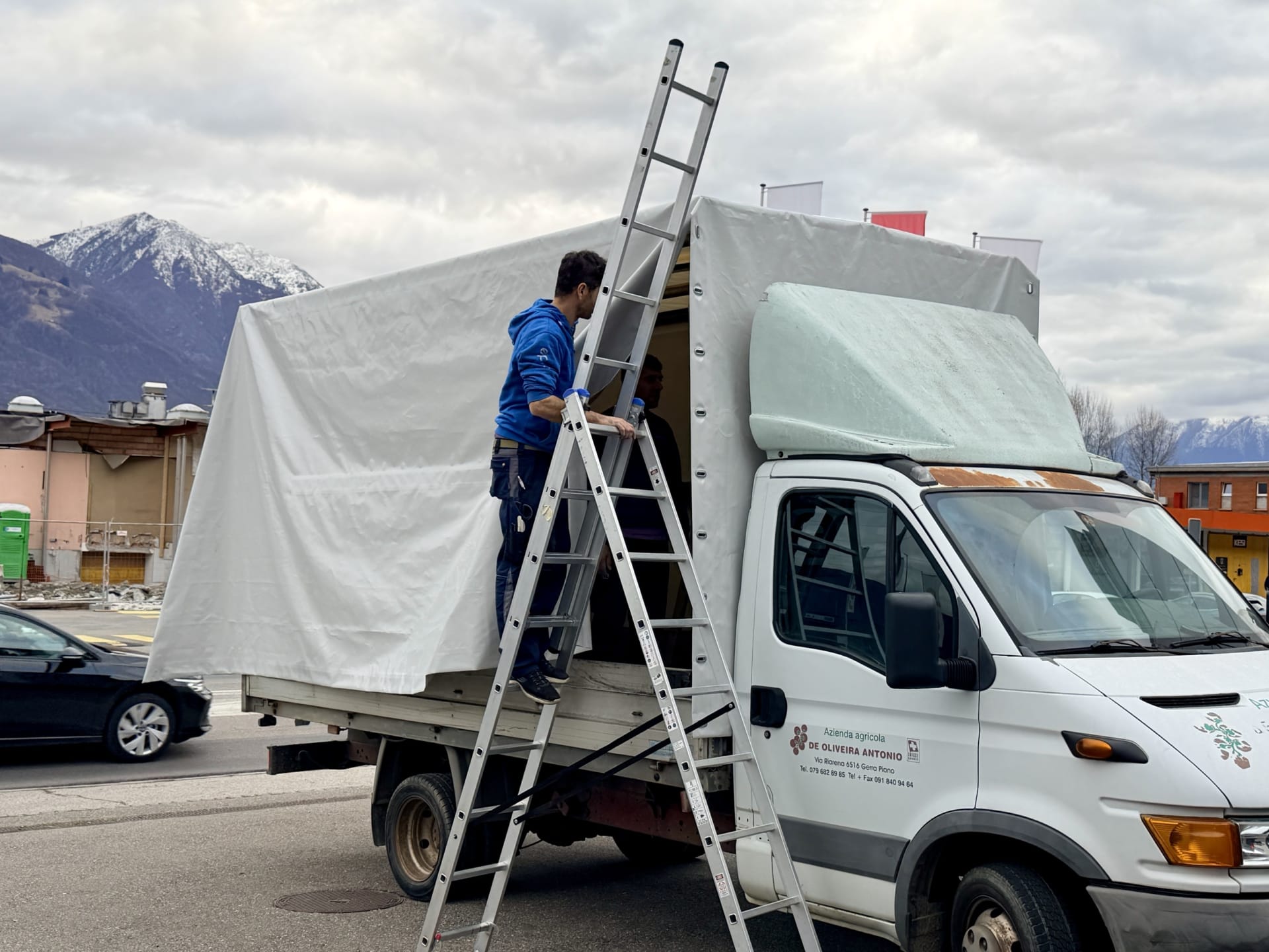 Montaggio di un telone su misura sul cassone di un autocarro, davanti al laboratorio
