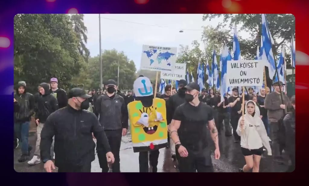 Ossi Ketola in a Freakbob mascot costume among masked marchers carrying Finnish flags in Helsinki