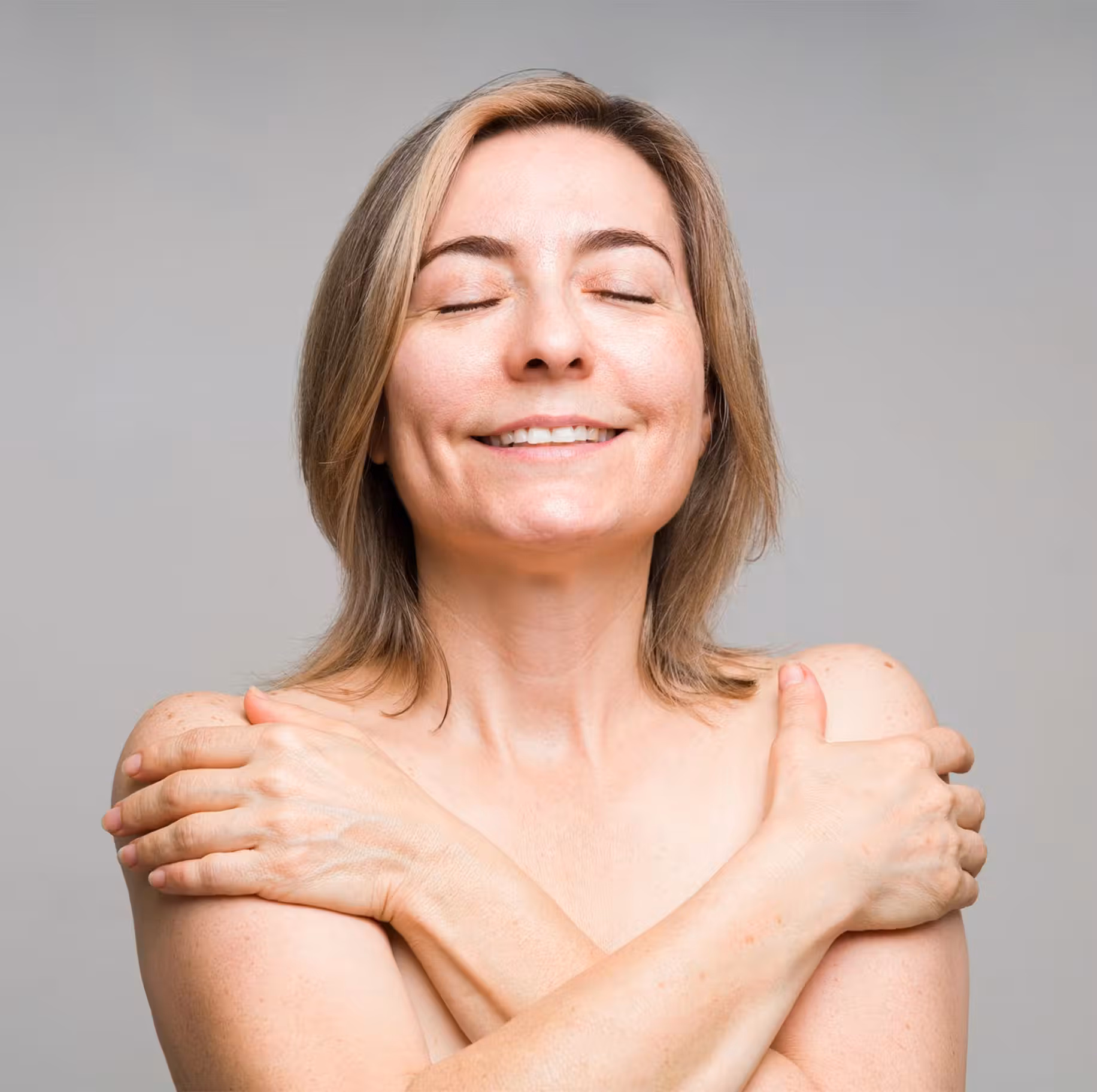 smiling woman with no shirt on crossing her arms to cover her breasts