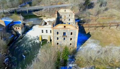 Аерофото водяного млина Потоцьких у Печері, Вінницька область. Стара будівля біля річки з порогами та мостом на задньому плані.