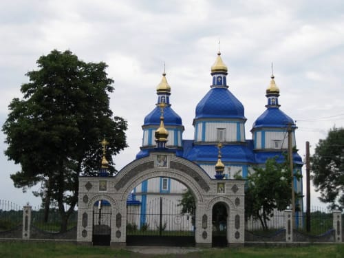 Церква Різдва Пресвятої Богородиці в селі Печера, Вінницька область, Україна. Дерев'яна церква з синіми куполами та золотими хрестами.