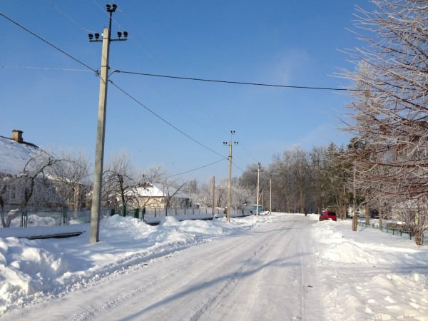 Засніжена сільська дорога в Печері, Вінницька область, з будинками, деревами в інеї та стовпами електропередач під блакитним небом
