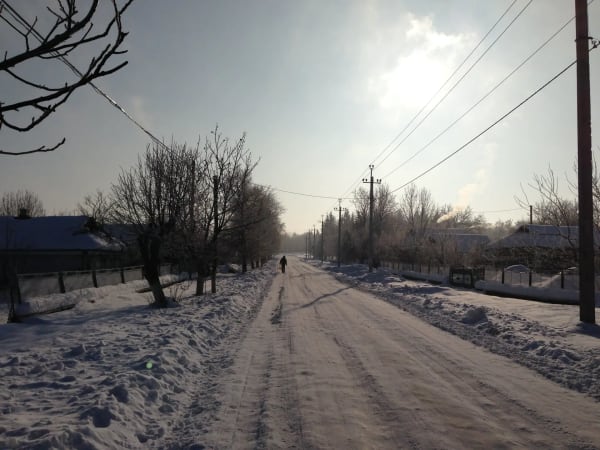 Зимова дорога в селі Печера, Вінницька область. Засніжена вулиця, дерева без листя, сонце на горизонті, людина йде по дорозі.
