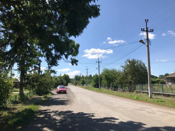 Широкий план сільської дороги в селі Печера, Вінницька область, з червоною машиною, деревами та стовпами електропередач.