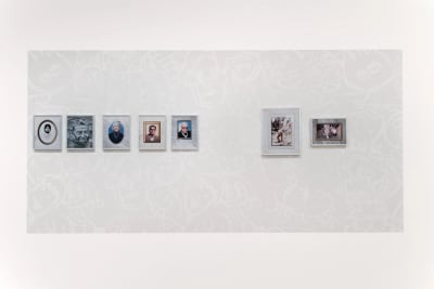 Group of framed colour inkjet photos hung on black and white wall painting consisting of stenciled graffiti faces.