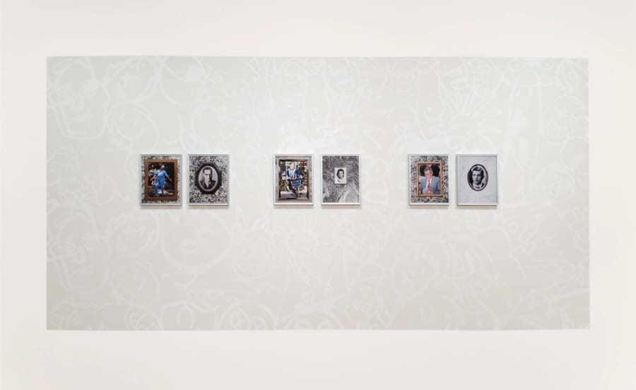 Group of framed colour inkjet photos hung on black and white wall painting consisting of stenciled graffiti faces.