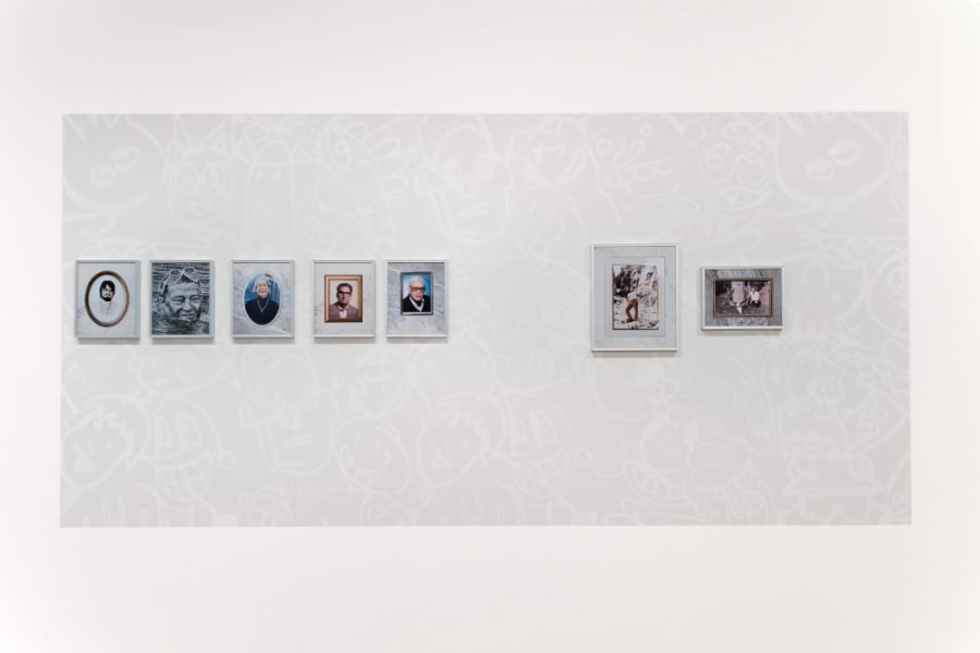 Group of framed colour inkjet photos hung on black and white wall painting consisting of stenciled graffiti faces.