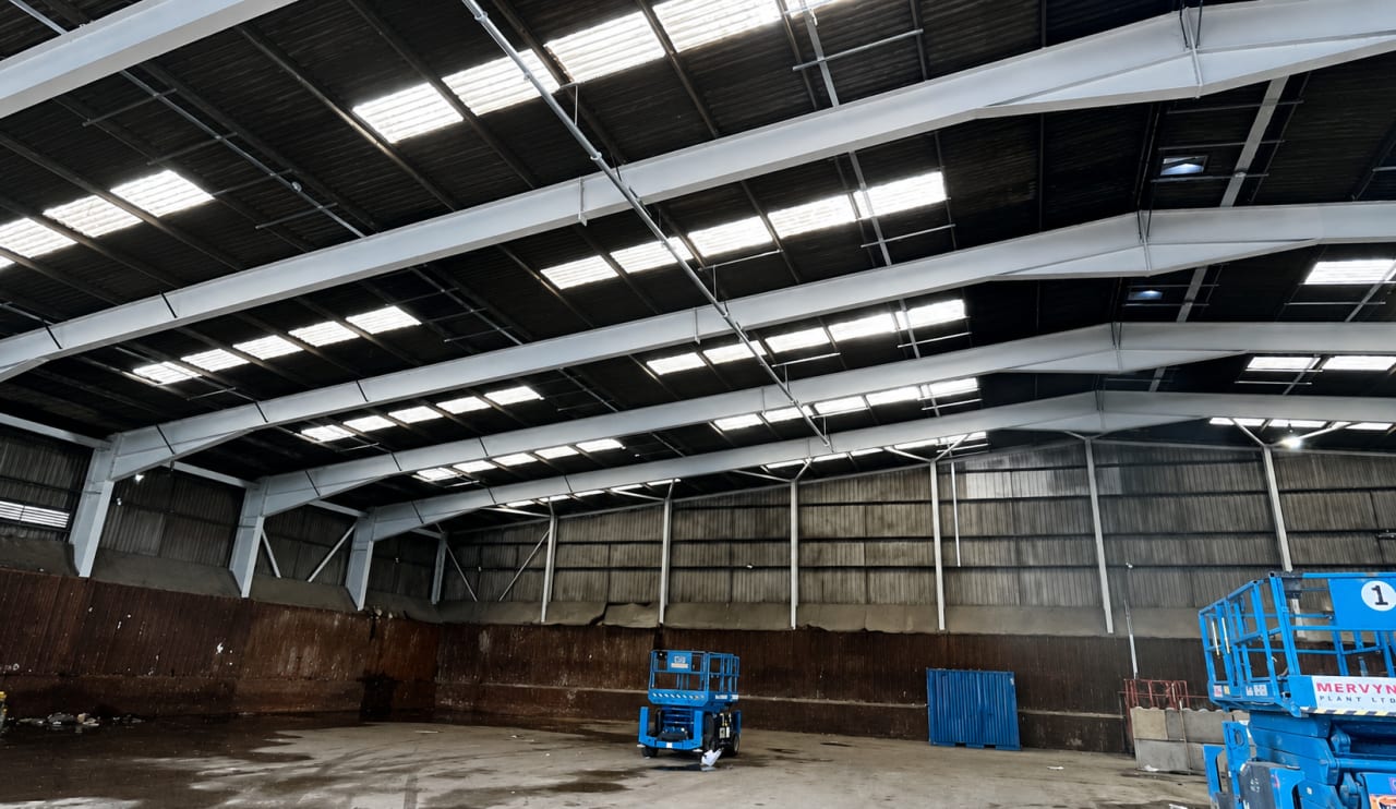 Empty warehouse interior with white painted roof steelwork, rooflights and a scissor lift.