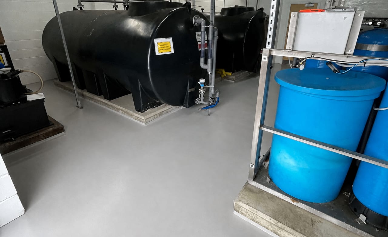 Plant room with black storage tanks and blue water tanks on a freshly coated grey resin floor.