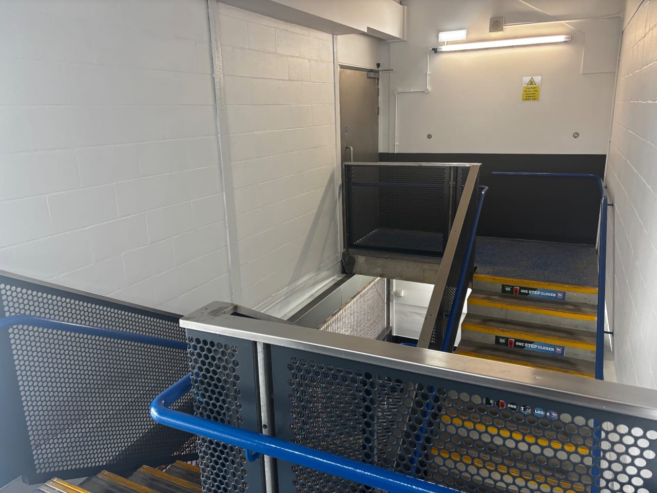 A stadium stairwell with freshly painted white walls, a grey base band, and refinished handrails and grilles.