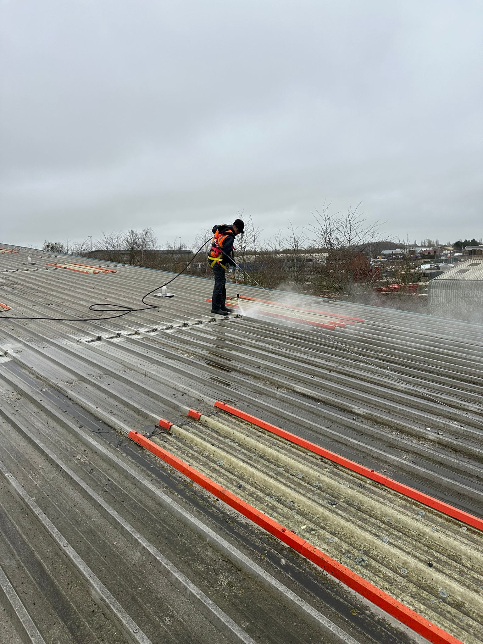 Operative pressure washing a profiled metal roof, with spray and run-off visible on the sheets.