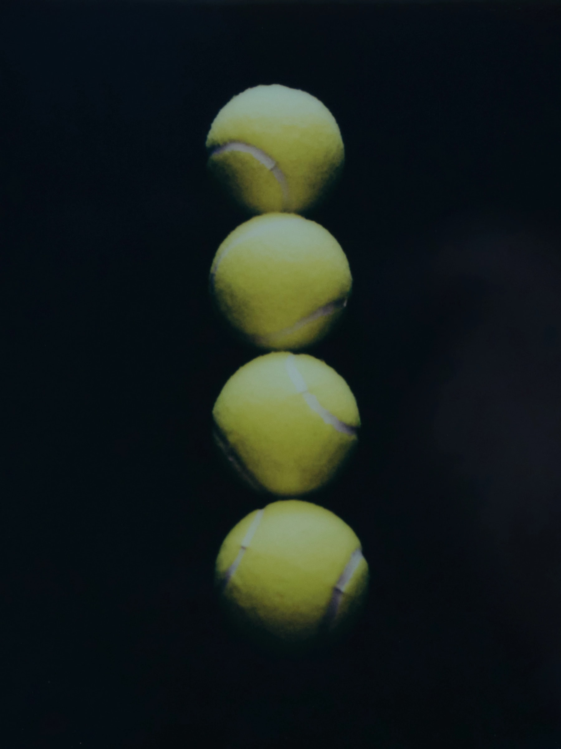 Four dimpled tennis balls stacked in a vertical column against black.