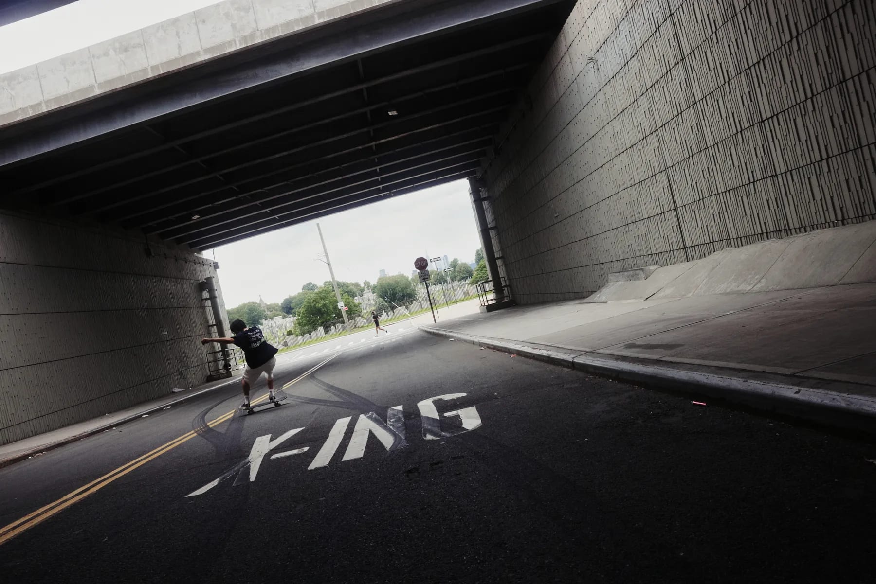 A skateboarder rolling through a highway underpass, FINS painted across the asphalt.