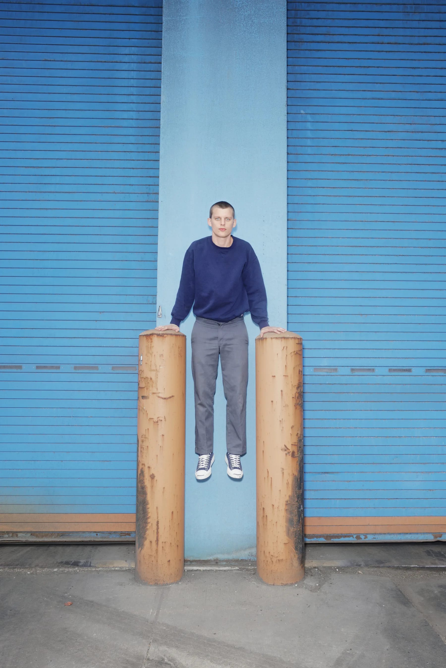 A figure standing on two upright wooden posts in front of a blue corrugated garage door.
