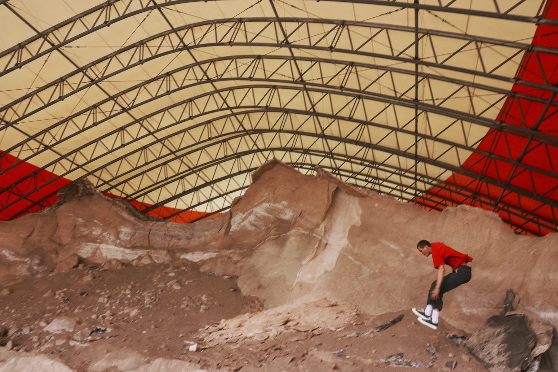 A small figure in red crossing the rubble beneath the canopy.