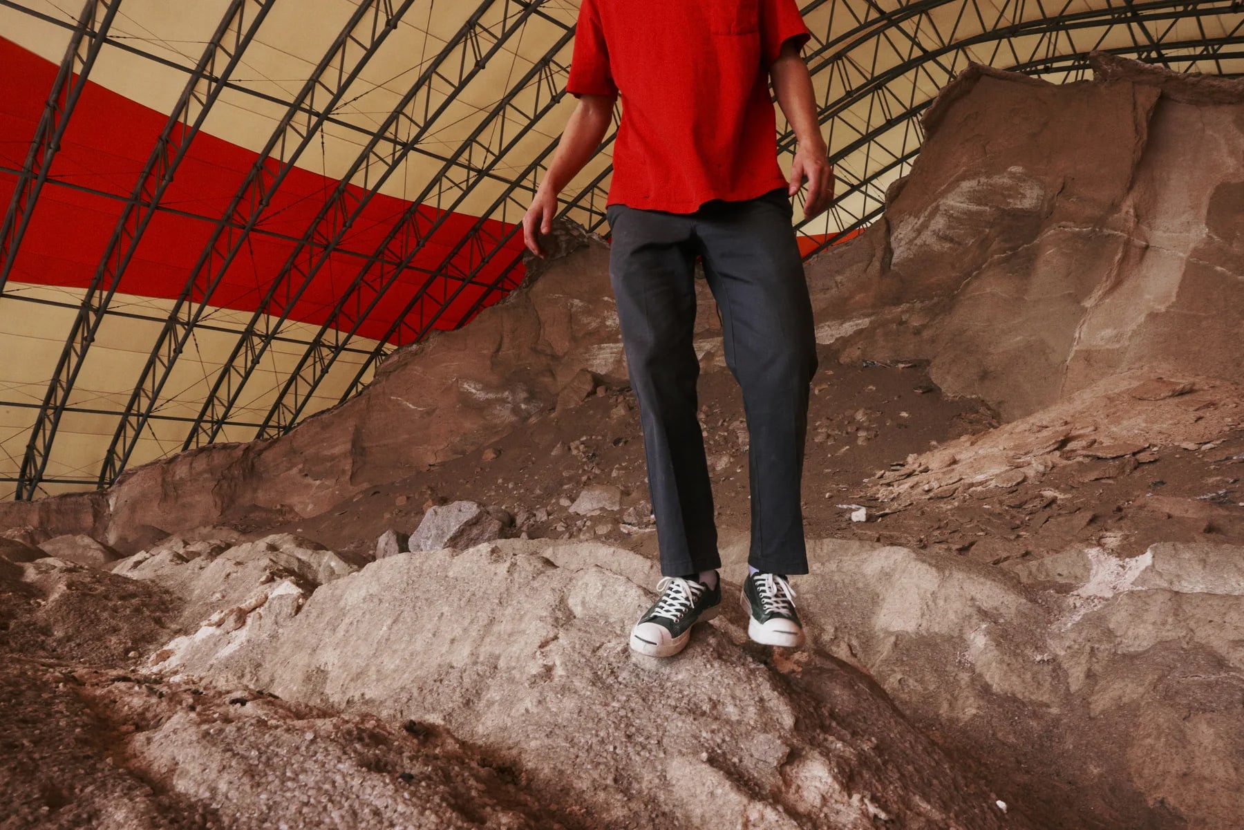 A close crop of legs and sneakers standing on the rubble, red shirt above.