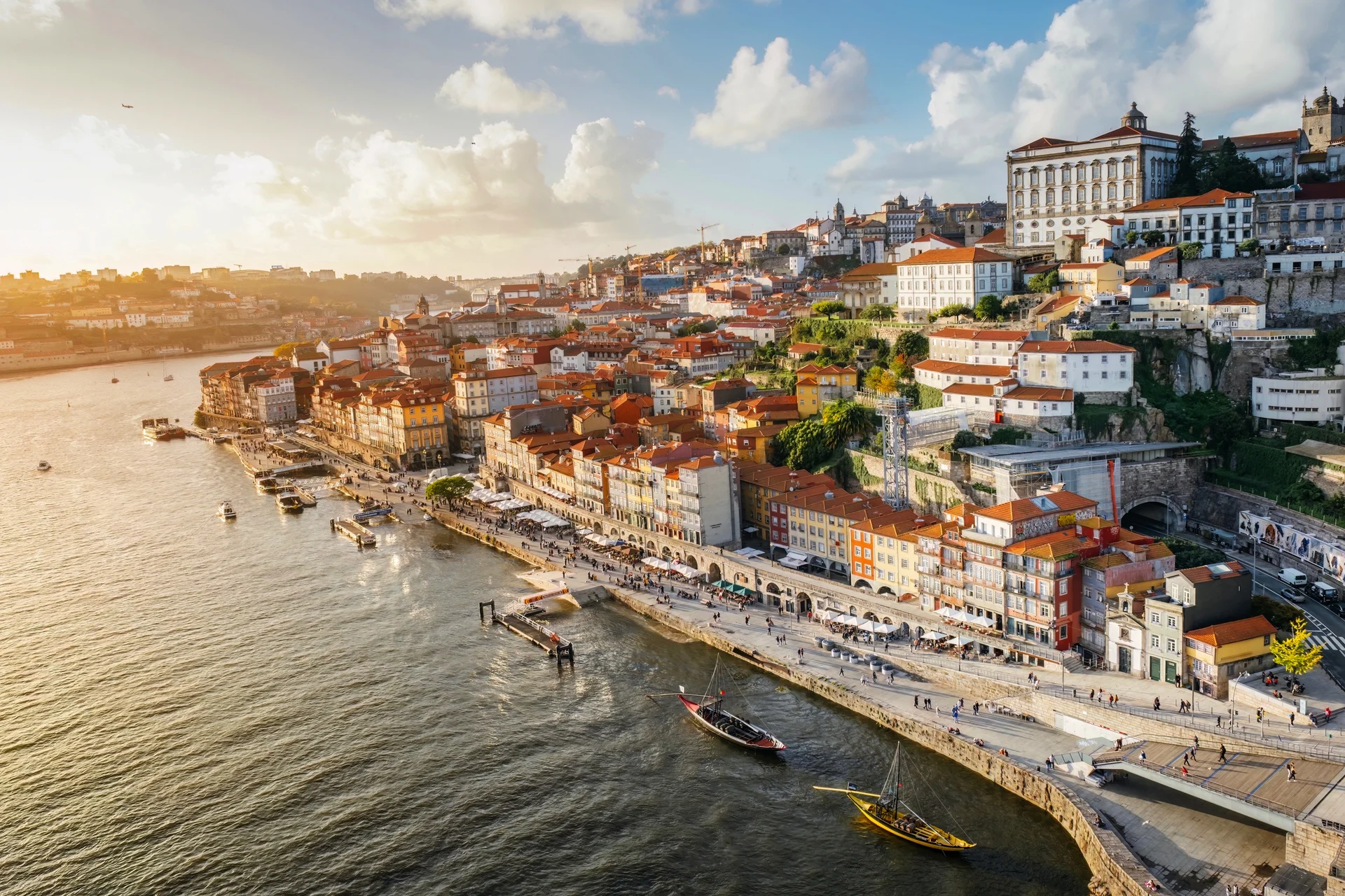 Stadtansicht mit Fluss und Hügelhäusern bei Sonnenuntergang.