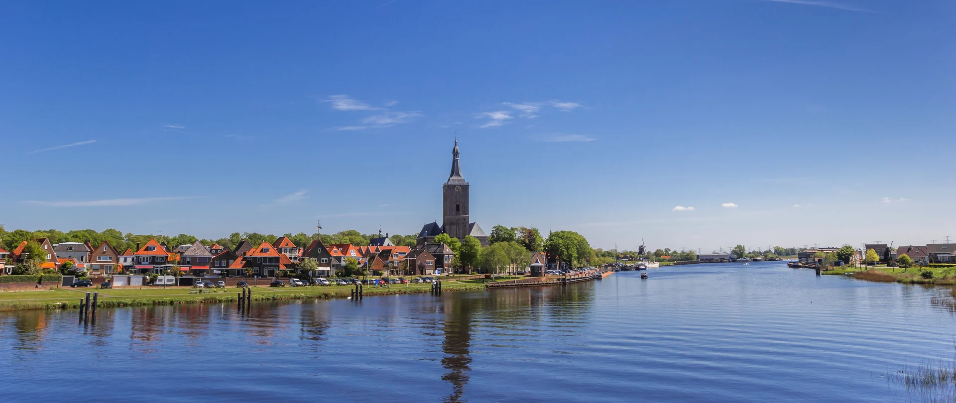Flusslandschaft mit Stadtansicht und Kirchturm im Hintergrund bei klarem Himmel.