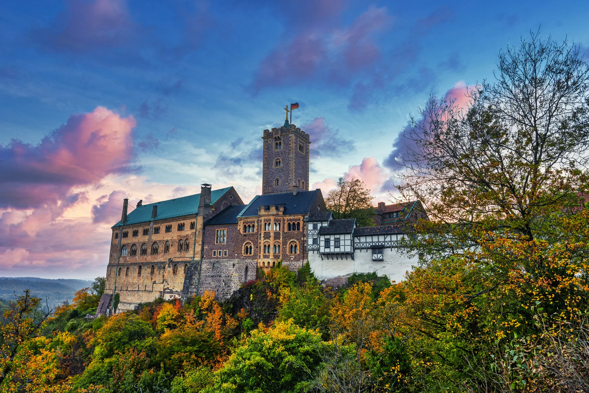 Burg auf einem Hügel bei Sonnenuntergang, umgeben von Herbstbäumen.