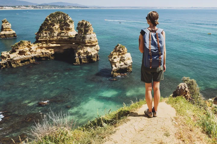 Person auf Klippe mit Blick aufs Meer und Felsformationen.