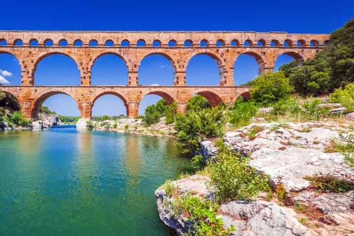 Römisches Aquädukt über einem Fluss mit bewaldeten Ufern und klarem, blauem Himmel.