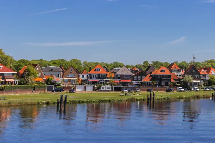 Flusslandschaft mit Stadtansicht und Kirchturm im Hintergrund bei klarem Himmel.