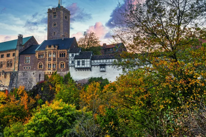 Burg auf einem Hügel bei Sonnenuntergang, umgeben von Herbstbäumen.