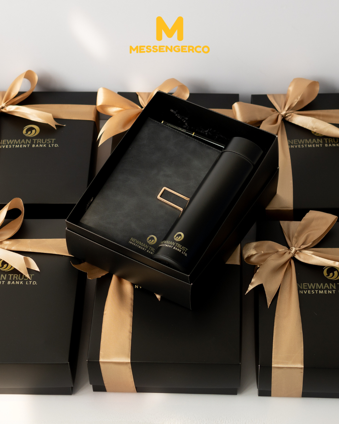 open corporate appreciation gift boxes with notebook and flask arranged on gold ribbon packaging
