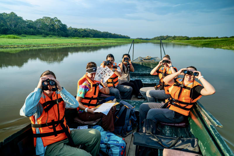 Students scan for wildlife with binoculars from a boat during Amazon fieldwork in Peru