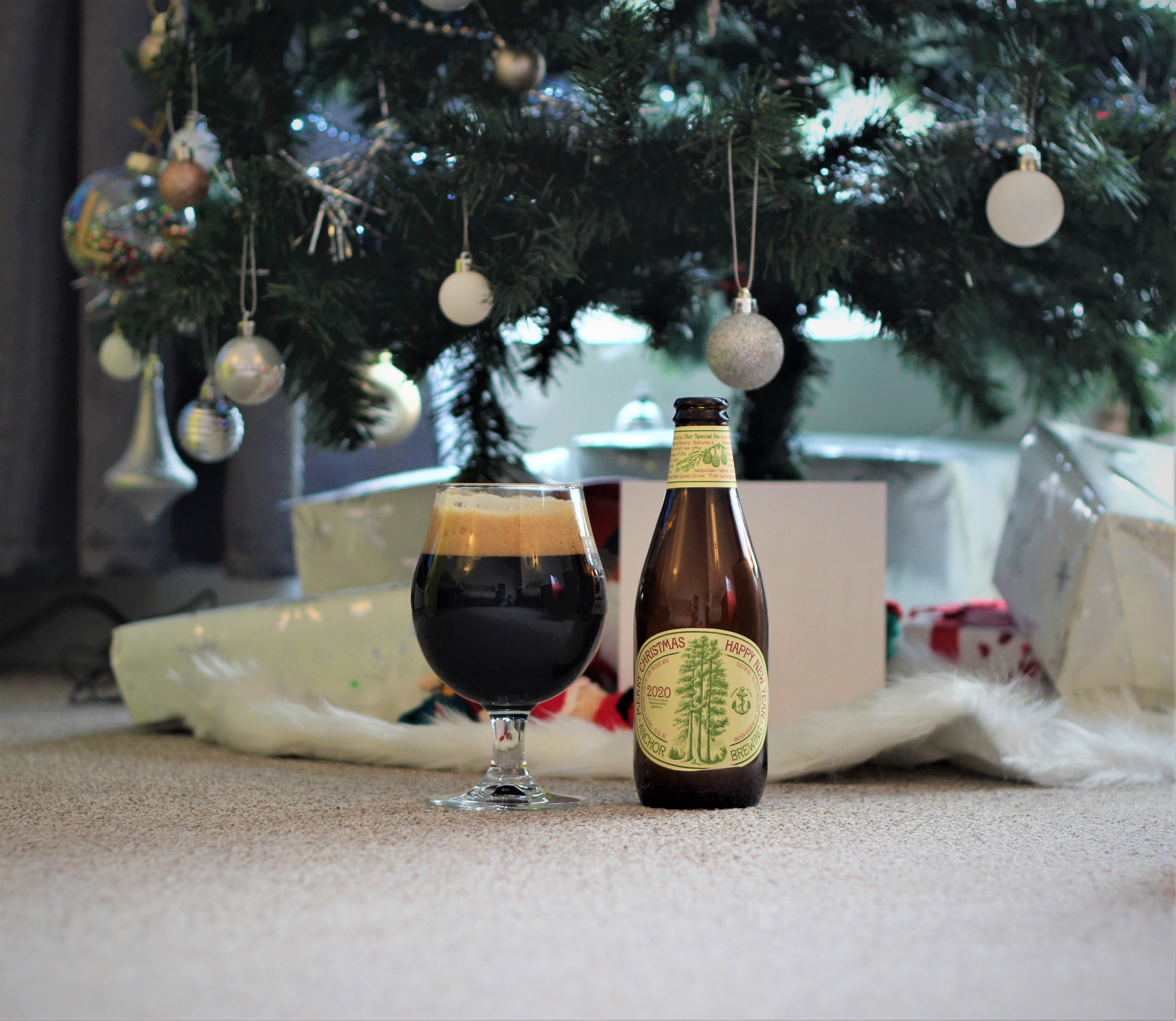 photo of anchor christmas beer in a glass next to the bottle with a christmas tree in the background