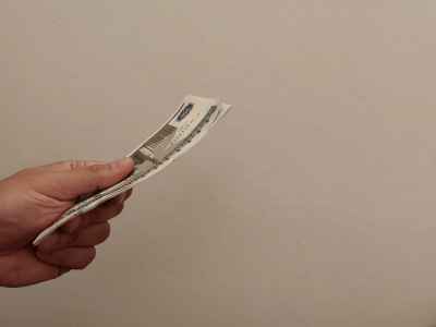 Hand Holding Cash Banknotes Against Plain Background